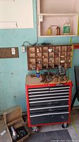 View of the Sears Craftsman red and black rolling tool chest with tools on top and small hardware on the wall shelf above it.