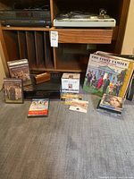 Photo showing the Technics turntable on a stereo shelf with vinyl records, CDs, DVDs, and VHS tapes placed below and in front of it.