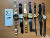 7 wristwatches arranged side by side on wooden surface showing overall lot