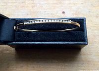 Full bangle resting in black velvet display box, showing overall design and diamond bar.