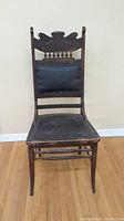 Front view of antique wooden chair showing carved backrest and black upholstered back and seat panels.