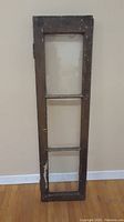 Front view showing full length of antique wooden window frame with chipping brown paint and three sections