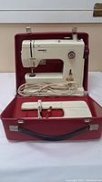 Front view of Bernina Minimatic sewing machine seated in red carrying case with power cord and extension table