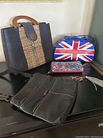 Roots black leather crossbody bag with adjustable strap, British flag handbag with wooden handles, and Desigual wallet arranged on a surface.