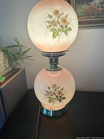 Front view of the double globe lamp showing both frosted glass globes with floral decoration and metal base.