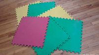 Six interlocking foam floor mats arranged on a wood floor, showing colors and shape (red, green, yellow).