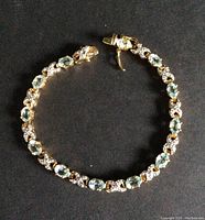 Full view of gold washed sterling silver bracelet with evenly spaced aquamarine stones on a black background.