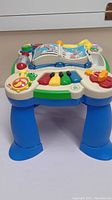 Image showing side view of the LeapFrog play table with colorful piano keys, spinning book, and large blue legs.