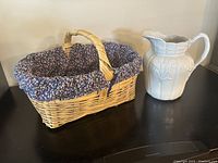 Wide shot showing both the wicker basket with floral cloth liner and white ceramic wheat sheaf pitcher side by side.