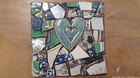 Photo of square mosaic artwork showing broken crockery pieces in various colors with a central blue ceramic heart.