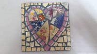 Front view of square mosaic showing heart motif created with broken patterned crockery pieces in multi-color floral patterns surrounded by pink and cream tiles with gray grout.