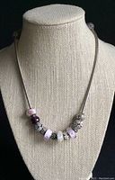 Full-length view of necklace and charms displayed on beige bust