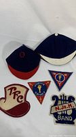 Two wool beanies and five embroidered patches arranged on a white surface, showing school insignias and band patch
