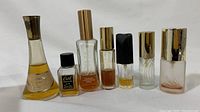 Photo shows seven vintage perfume bottles arranged side by side, displaying variety in shape, size, and color, with worn metal caps and varying levels of perfume residue.