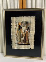 Framed Egyptian print centered on black background with visible wood frame in gold and silver tones.