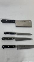 Four Zwilling JA Henckels kitchen cutting utensils laid out on white surface including a cleaver, serrated knife, and two straight edge knives