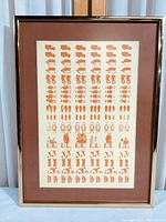 Full view of the framed abstract print showing farm-related repetitive icons in burnt orange on white, with a brown mat and gold metal frame.