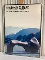 Framed poster print showing a sculpture in outdoor setting with mountain background, title text in Japanese and English at top.