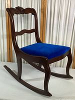 Side view of small vintage wooden rocking chair showing royal blue velvet upholstered seat and curved rockers.