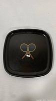 Front top view of vintage Couroc black tennis platter with crossed rackets and tennis balls illustration.