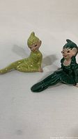 Two ceramic pixie elf figurines, one lime green and one dark green, on white background