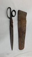 Vintage metal shears alongside their worn leather sheath.