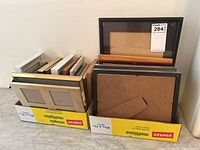 Two boxes filled with various sizes and colors of picture frames, stacked vertically showing front and back sides.