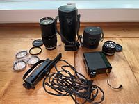 Overview of all items in lot including lenses, carrying cases, filters, flash unit, and accessories on wooden surface.