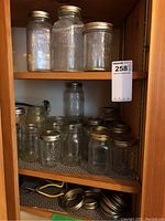 Bottom shelf with multiple medium and small mason jars with metal lids; some jars are shorter and some taller, all clear glass with wear.