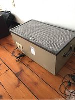 Side view of the Tibbits Clean Air Machine PC260 with mesh top and power cord visible, showing metal casing and handles.