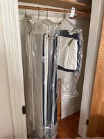 Wide view of two large drapes, valance, and tablecloth hanging on hangers covered in clear protective plastic bags.