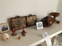 Wide view of all items on white surface, showing layout and grouping of plaques, ceramic sheep, wooden cardinal, rabbits, framed art pieces, and wood bowls.