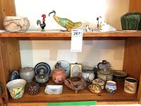 Wide view of assortment of pottery items placed on wooden shelves showing bird figurines, pots, jars, planters and a small ceramic dish.