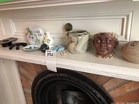 Shelf showing assorted small ceramic decorative items including rabbit flower holder, ceramic plates, cups, small vases, and two figurative ceramic pots.