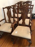 Eight wooden dining chairs arranged in two rows: two armchairs with carved arms in front and six side chairs behind. Upholstered seats in beige fabric. Carved wooden backs with decorative top rail and queen anne legs.