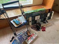 Photo of the Exer-Cor NordicTrack Chair Gym sitting against a window with several workout accessories including ankle weights, jump rope, vintage chest expanders, pink dumbbells, and booklets arranged around it.