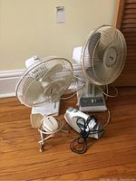 Three electric fans and one Black & Decker steam iron placed on wooden floor, showing general condition and cords.