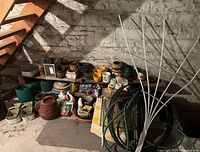 Wide view of assorted garden planters, watering can, hose, garden edging, and other gardening items arranged on shelves and floor against stone wall