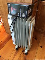 Noma electric radiator heater showing front side with control knob and power cord, situated next to the boxed Conair hair dryer.