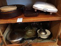 Shelf with white waffle maker, dark brown glass baking dishes, and woven hot plate coasters