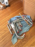Folded aluminum ladder parts with curved hooks and red end caps, laid on blue cloth on wood floor.