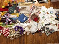 Overview of embroidered linens such as napkins, placemats, doilies, aprons, braided cords, and decorative small items spread out on wooden floor