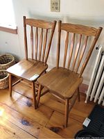 Pair of solid wood dining chairs placed side by side on wood floor, showing front and side angles.