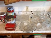 Full view of glass serving ware on countertop with several Christmas tins to the left.
