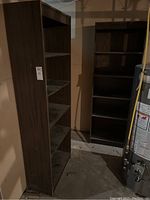 Pair of dark woodgrain pressboard shelving units side by side in basement, showing full height and shelves