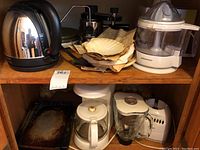 Shelf showing stainless steel electric kettle, Juiceman juicer, coffee filters, white coffee maker, and glass blender