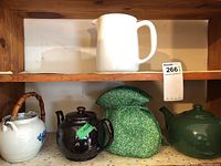 Five teapots and tea cozy arranged on shelf showing variety and styles