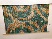 Full view of large textile wall hanging displayed on white wall showing tie dye pattern, wooden dowels, and overall dimensions.