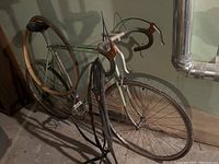 Side view of the full vintage Peugeot road bicycle leaning against a wall, showing flat rear tire and spare inner tubes hanging.