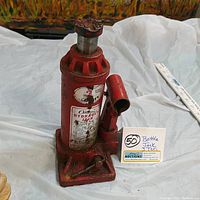 Full view of red hydraulic bottle jack showing cylindrical body, attached valve, and height scale nearby for measurement.